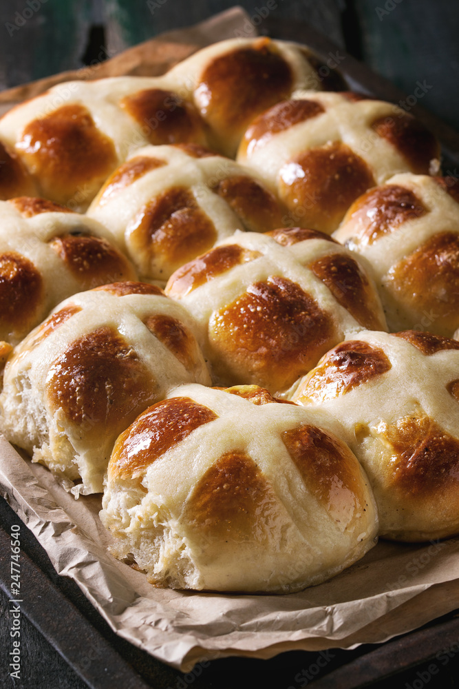 Homemade Easter traditional hot cross buns on oven tray with baking paper over dark wooden background. Close up Homemade Easter traditional hot cross buns on oven tray with baking paper over dark wooden background. Close up