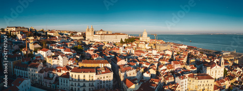 Aerial drone view of old city roofs; sunny evening in Portuguese capital, golden sunlights and dusk shadows on the ancient houses; beautiful cityscape with historical touristic routes and sunset sky