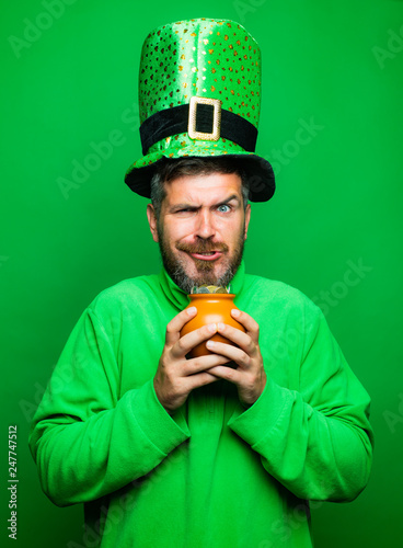 Man in Saint Patrick's Day leprechaun party hat hold Pot of gold on green background. Happy St Patricks Day concept with pot of gold. photo