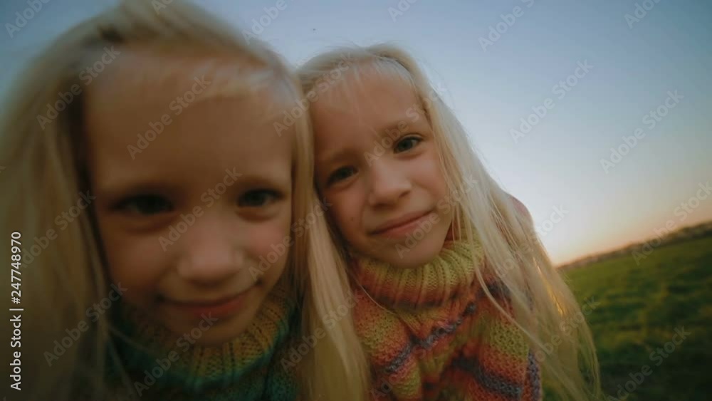 slow motion closeup happy little fair haired twin sisters look at camera on fresh field against clear sky slow motion closeup happy little fair haired twin sisters look at camera on fresh field against clear sky