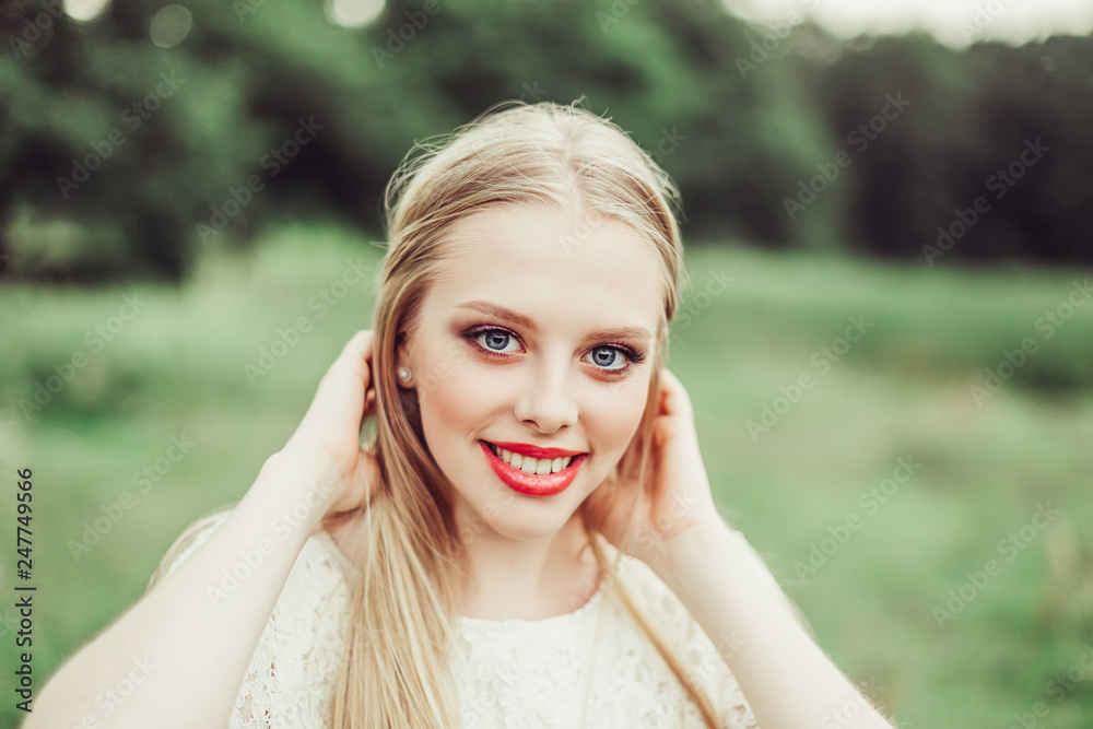 Close up natural portrait of young happy cute cheerful caucasian beautiful girl witn long natural blondie hair walking in park in summer evening