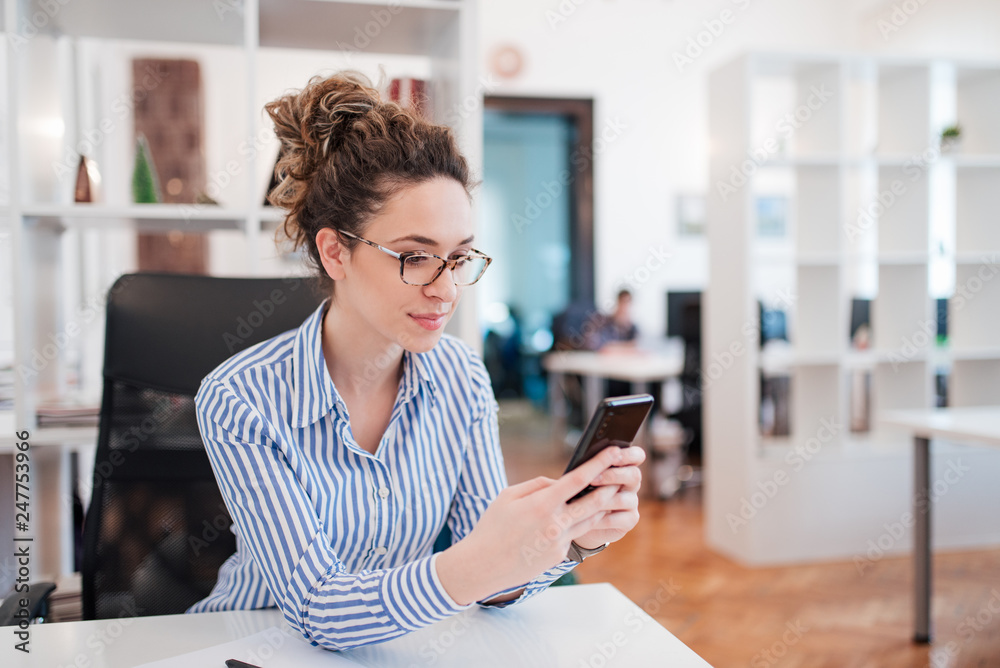 Beautiful young office worker texting on smart phone.