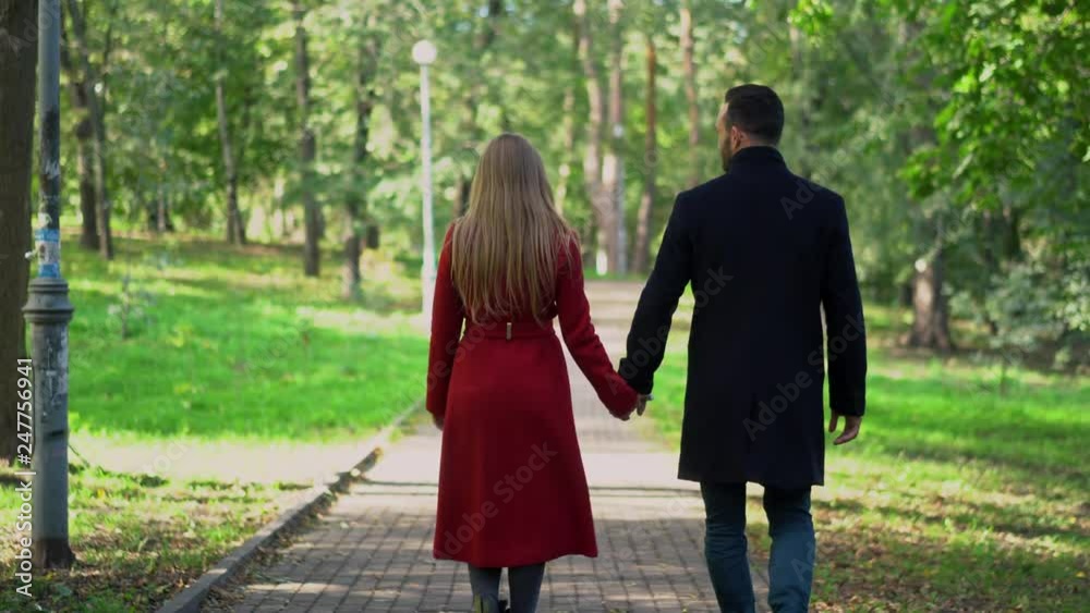 Loving couple holds hands while walking in the park. Loving couple holds hands while walking in the park.