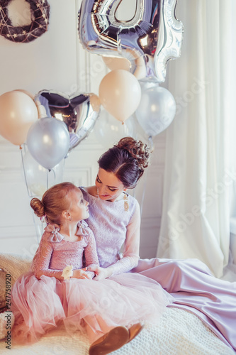 Close up portrait of elegant stylish mother and daughter in fashion dresses playing together, celebrating happy birthday. Baloons background, party concept. Childhoood, cute kid, carefull mother photo