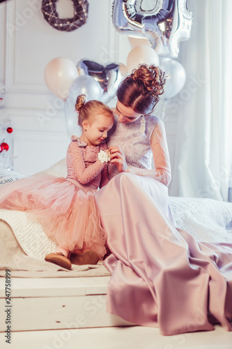 Close up portrait of elegant stylish mother and daughter in fashion dresses playing together, celebrating happy birthday. Baloons background, party concept. Childhoood, cute kid, carefull mother photo