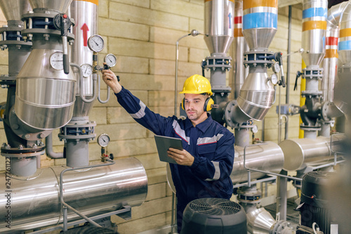Obraz na plátně Young Caucasian worker in protective suit tightening the valve and using tablet while standing in heating plant
