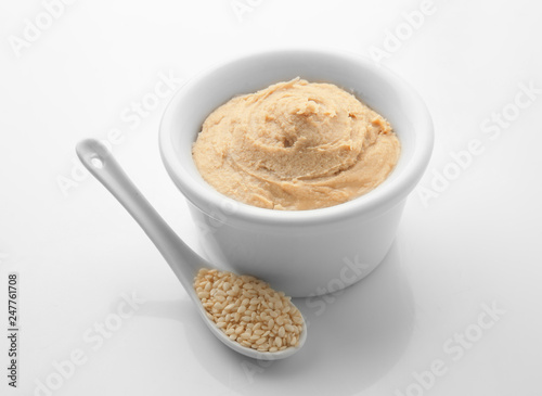Bowl of tasty tahini with sesame seeds on white background © Pixel-Shot