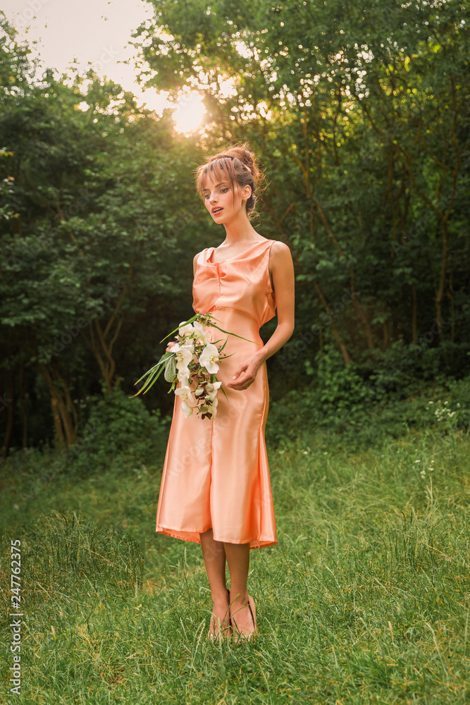 The beautiful young lady in the dress standing in the garden and holding the flowers in hands
