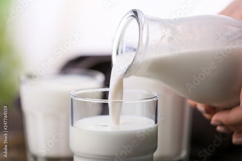 Fotografie Pouring of fresh milk from bottle into glass, closeup