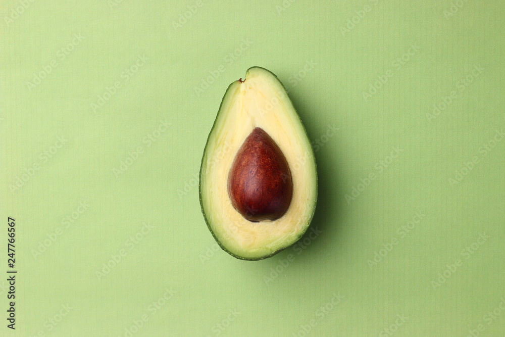 half avocado with seed on a green background top view