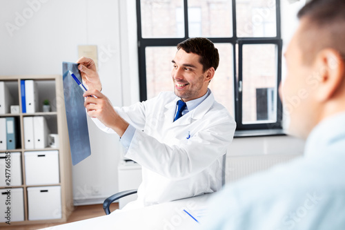 medicine, healthcare and people concept - smiling doctor showing x-ray to patient at medical office in hospital