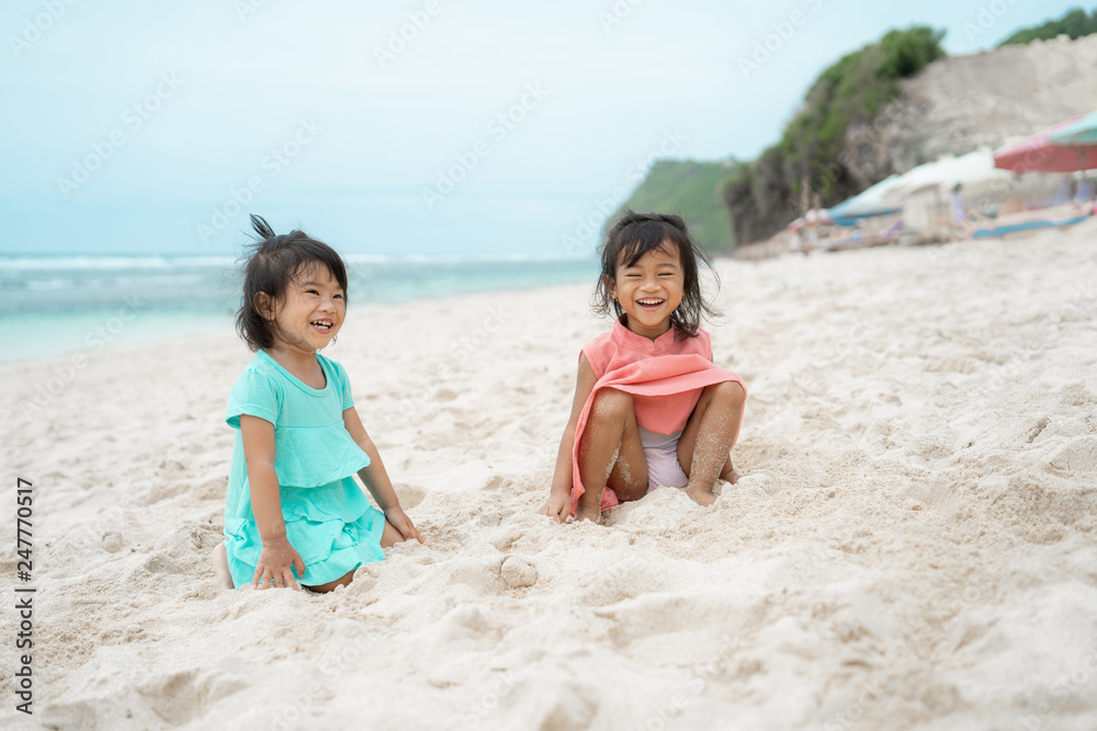 two daughter sit down on white sand smiling at the camera two daughter sit down on white sand smiling at the camera