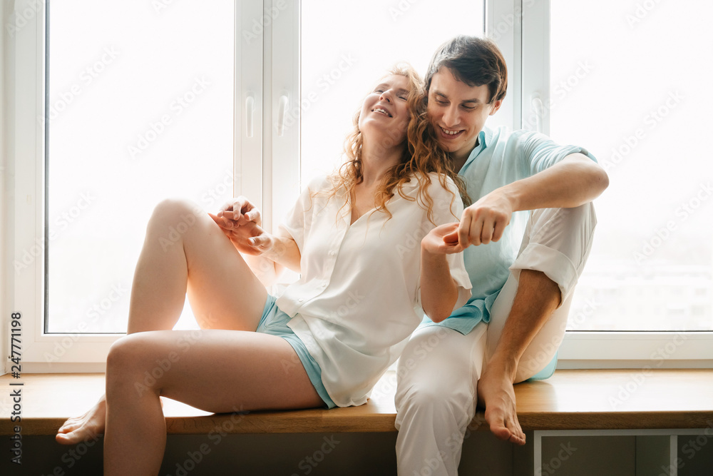 Happy girl and man hugging near window in home. 