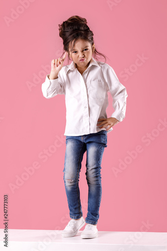 Tablou pe pânză angry little child girl in white shirt with hairstyle looking to camera on pink background