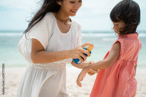 application sunblock to daughter skin before playing on the beach to protect from sun beath photo