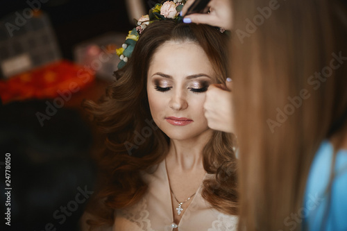 A makeup artist applies bright wedding makeup for the beautiful brunette model girl with stylish wedding hairstyle, wedding preparation of the young bride