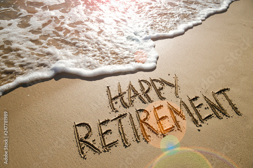 Happy Retirement message handwritten on smooth sand beach with gentle wave photo