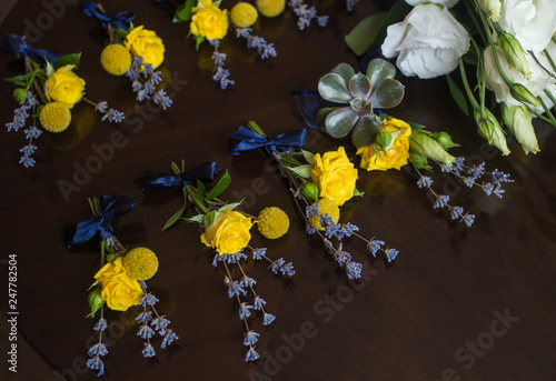 Closeup view of several small wedding floral boutonnieres made with yellow roses and violet flowers isolated on dark background. Horizontal color photography. photo