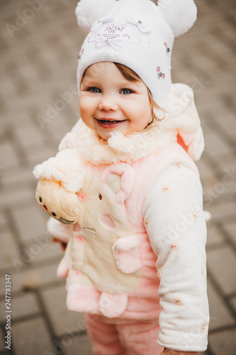 Portrait of happy smiling little girl wearing in white hat like mikey mouse walking in yard and playing, looking and turned at camera. Pretty child laughing and having fun outdoors. photo