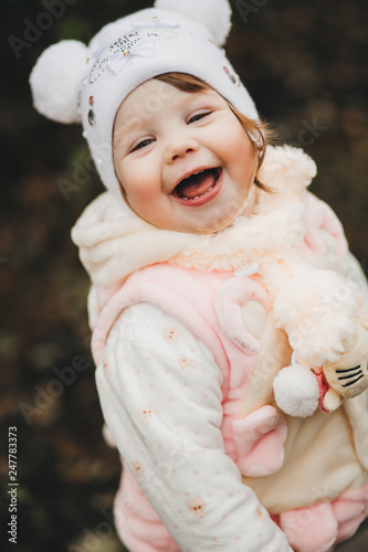 Positive smiling little girl looking  and turned at camera and laughing. Child playing at garden. Pretty kid wearing in white hat like mikey mouse and soft pink suit. photo