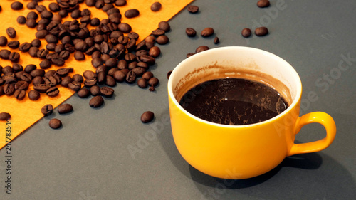 Yellow cup of coffee on a gray and yellow background with coffee beans