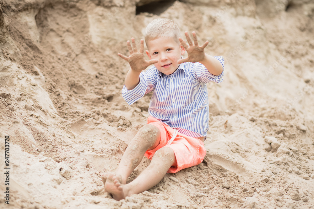 Portrait of cute happy white child showing his dirty sandy hands after playing with sand at river beach during summer weekend. Horizontal color photography. Portrait of cute happy white child showing his dirty sandy hands after playing with sand at river beach during summer weekend. Horizontal color photography.