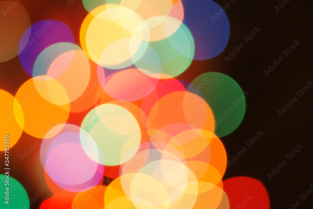 Multi-color holiday garland. Garland is blurred. Many colorful round lights. Fully defocused photo. Blurred background and foreground. Holiday mood. New Year and Christmas is coming.