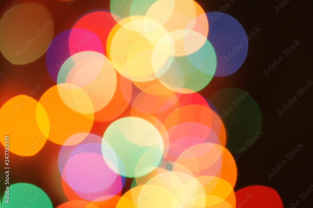 Multi-color holiday garland. Garland is blurred. Many colorful round lights. Fully defocused photo. Blurred background and foreground. Holiday mood. New Year and Christmas is coming.