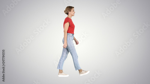 Woman in red t-shirt, jeans and sneakers walking on gradient background.