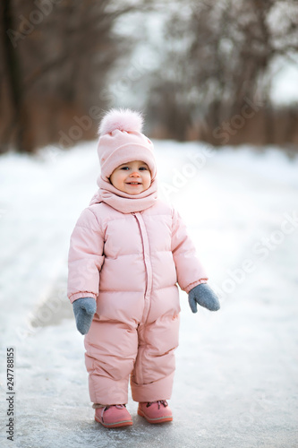 Little beautiful girl in pink jumpsuit in a snowy winter park