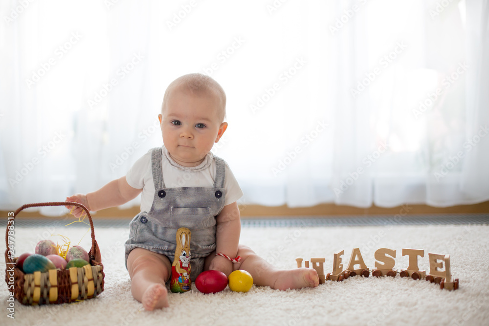 Fototapeta premium Cute little toddler child in sunny living room playing with Easter chocolate bunny and colorful Easter eggs