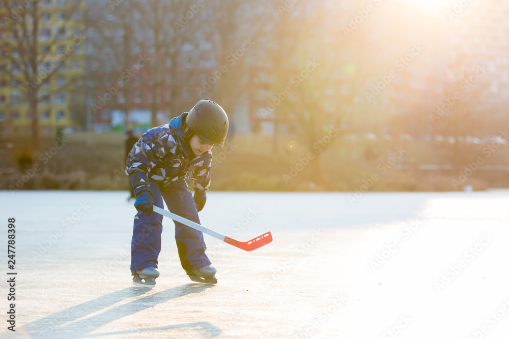 Naklejka premium Children, playing hockey and skating in the park on frozen lake, wintertime on sunset