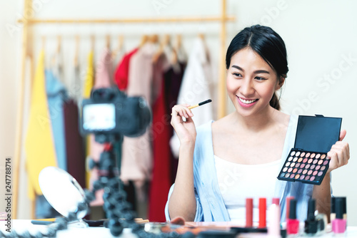 Portrait or headshot of attractive young asian influencer, beauty blogger, content creator or vlogger girl review make up looking at camera at home. Asian woman using internet for tutorial live video.