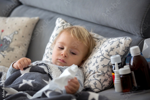 Sick child, toddler boy lying in bed with a fever, resting at home