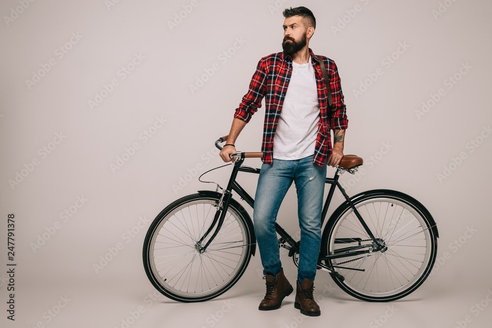 bearded man in checkered shirt standing at bike on grey bearded man in checkered shirt standing at bike on grey