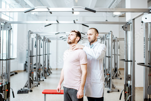 Professional senior physiotherapist doing manual treatment to a man standing in the rehabilitation gym