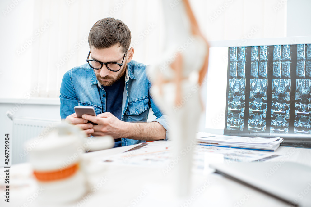 Man using smartphone sitting hunched down having scoliosis in the office of therapist at the clinic