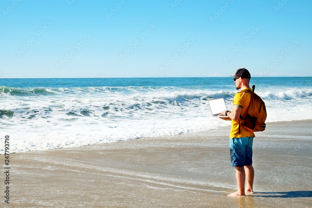 Fit travel blogger holding laptop, writing article on white laptop, standing on empty beach. Freelance remote work concept. Self employed man in yellow t-shirt coding. Copy space, sea view background. Fit travel blogger holding laptop, writing article on white laptop, standing on empty beach. Freelance remote work concept. Self employed man in yellow t-shirt coding. Copy space, sea view background.