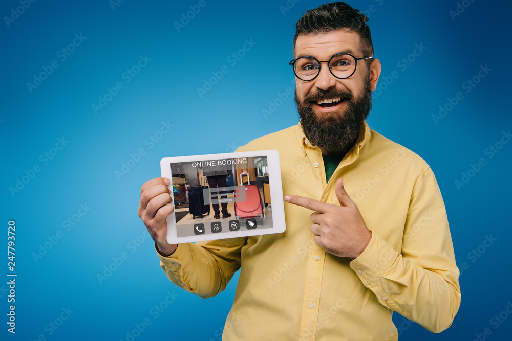 happy bearded man pointing at digital tablet with online booking app, isolated on blue happy bearded man pointing at digital tablet with online booking app, isolated on blue