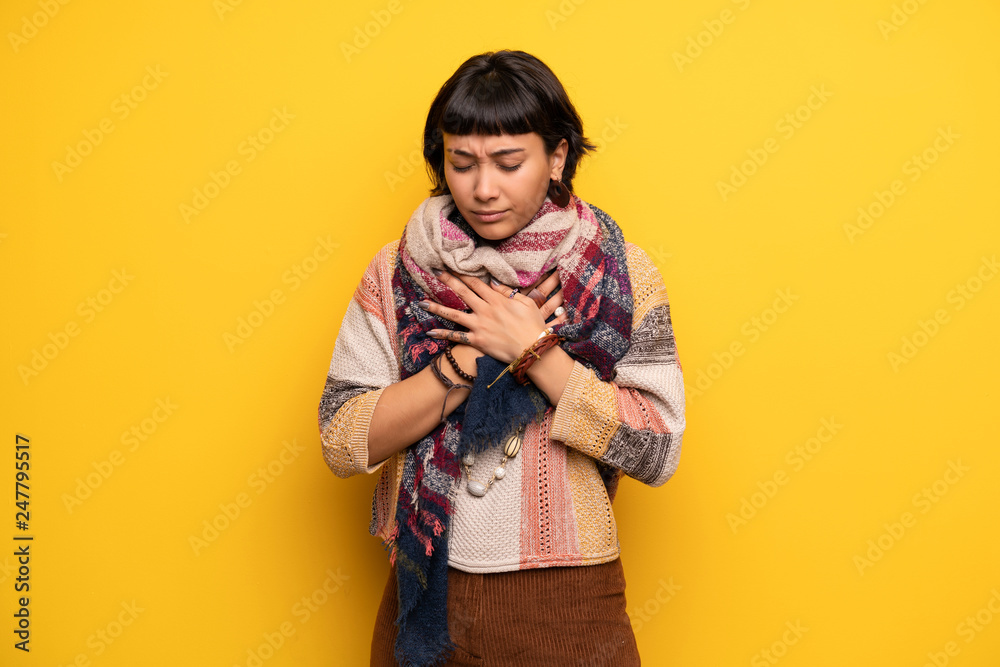 Young hippie woman over yellow wall having a pain in the heart Young hippie woman over yellow wall having a pain in the heart
