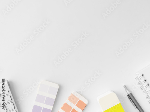 top view of Designer work space with notebook, keyboard, Color swatches book and Pencil on white background with copy space.