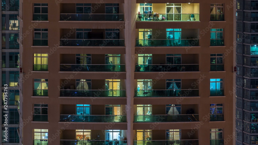 Glowing windows in multistory modern glass residential building light up at night timelapse.