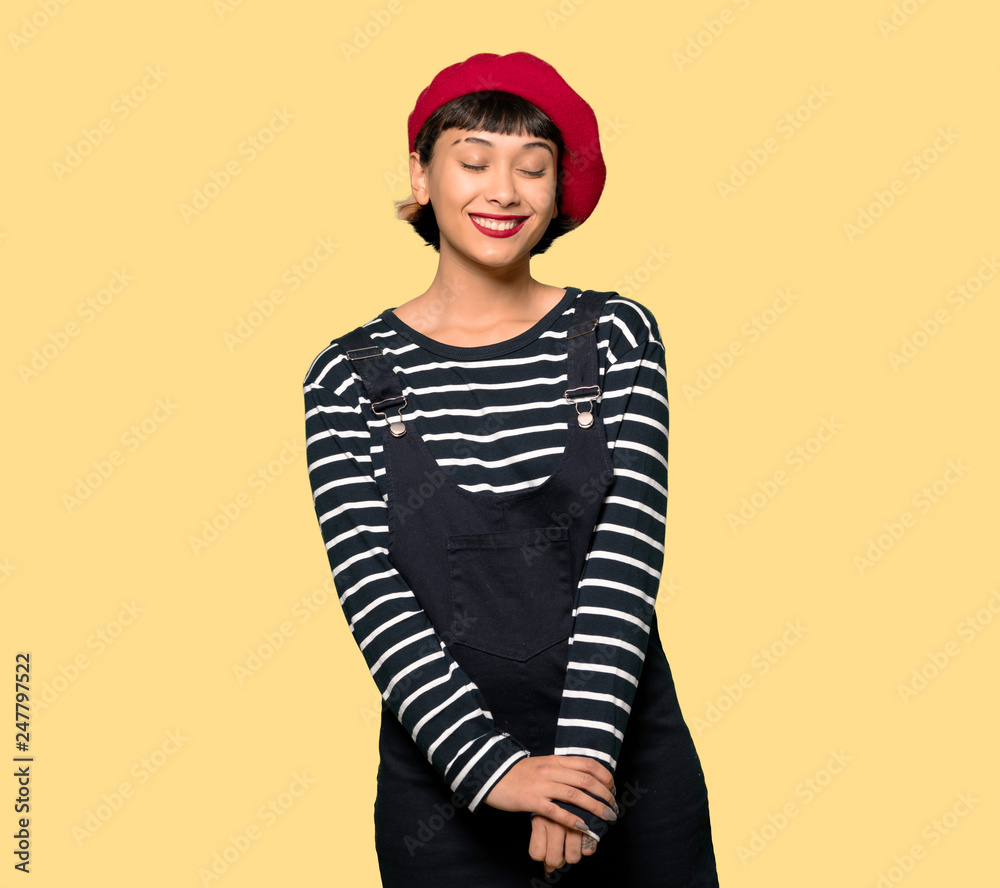 Young woman with beret keeping the arms crossed in frontal position over yellow background