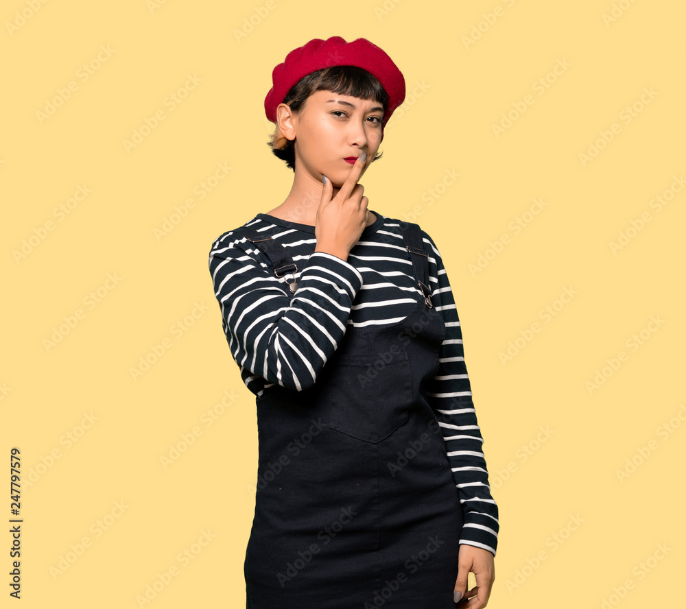 Young woman with beret covering mouth with hands for saying something inappropriate over yellow background Young woman with beret covering mouth with hands for saying something inappropriate over yellow background