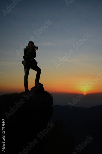 Dark silhouette of man photographer on the cliff and beauty sunrise in the morning.