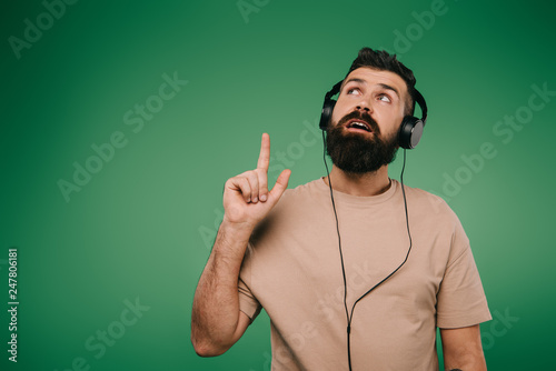 bearded man in headphones having idea and pointing up, isolated on green