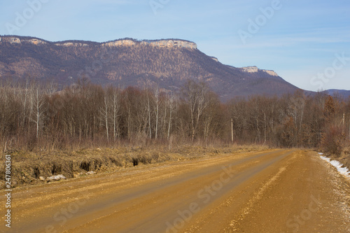 Beautiful pictorial landscape of stretching into distance of mountain road with trees outlines of powerful mountains under boundless blue sky in spring
