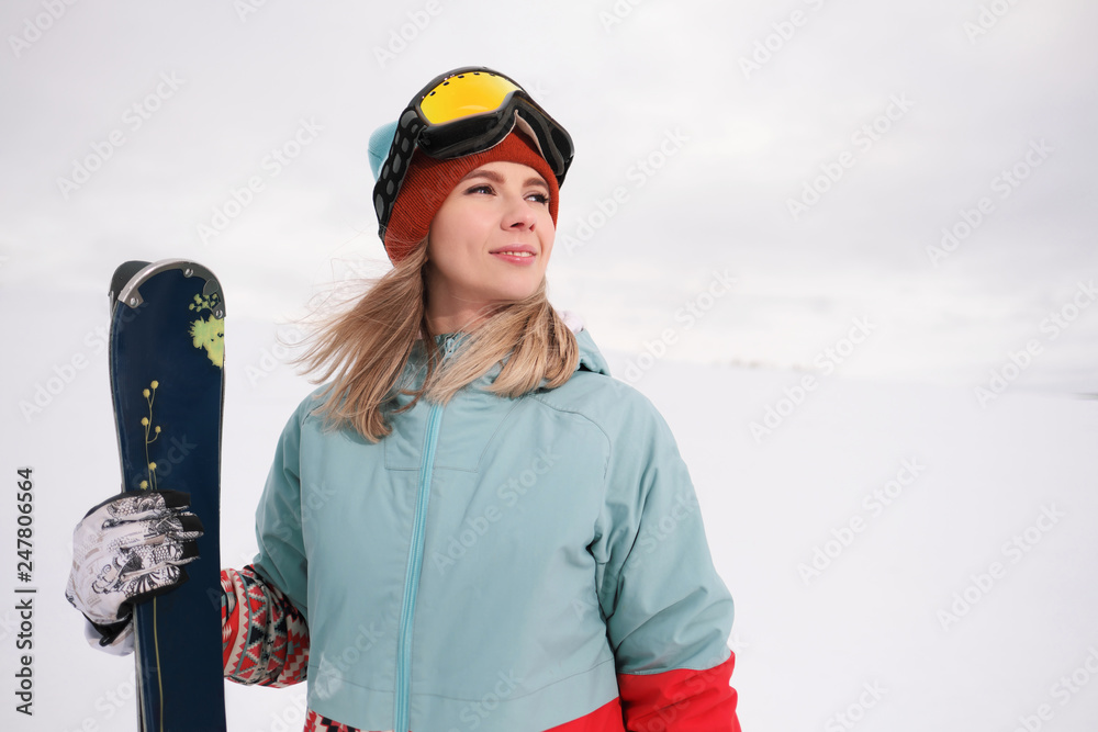 A beautiful young chew in an extreme sports suit, a hat and a helmet with a mask on the winter slope is holding alpine skis.