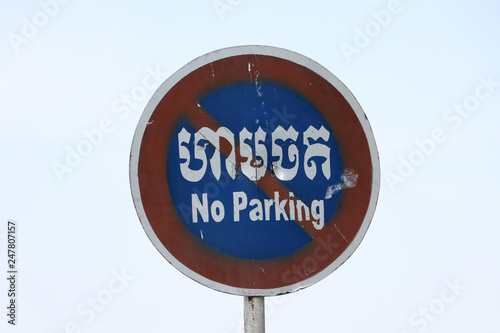 No Parking sign on sky background in Cambodian language and English.