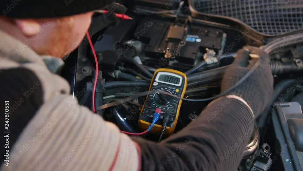 Car service. Thick mechanic man checks the voltage